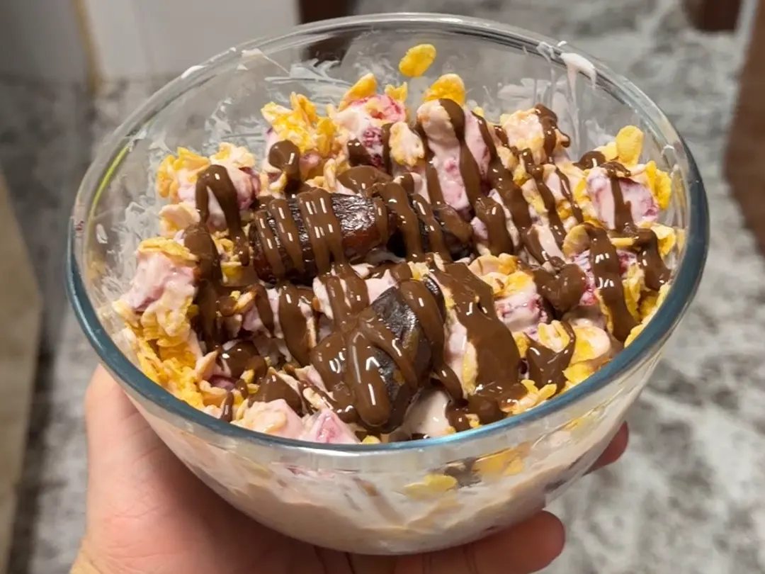 Bol de merienda con yogur griego, fresas, corn flakes y sirope de chocolate por encima