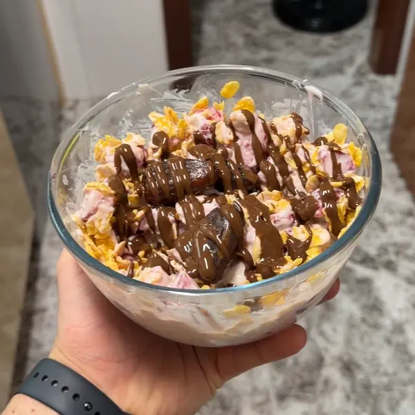Bol de merienda con yogur griego, fresas, corn flakes y sirope de chocolate por encima