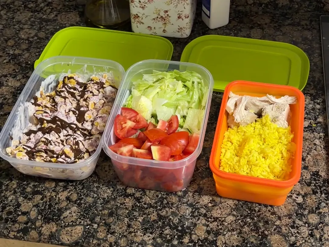 Tres táperes sobre la encimera: yogur con fresas y corn flakes, ensalada de lechuga y tomate, y arroz con pollo
