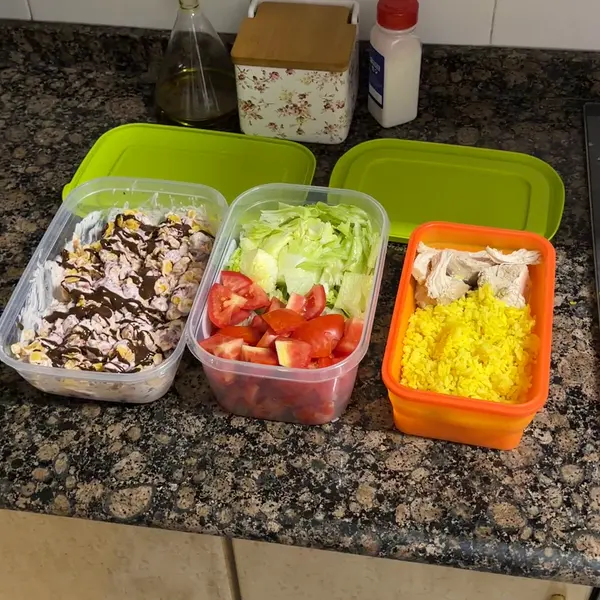 Tres táperes sobre la encimera: yogur con fresas y corn flakes, ensalada de lechuga y tomate, y arroz con pollo